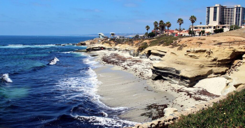 Ocean beach with cliffs, palm trees and buildings in the background, in La Jolla, CA