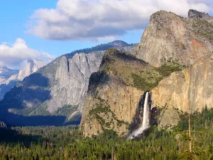 Scenic view of Yosemite Valley with towering granite cliffs and Bridalveil Falls cascading down, surrounded by lush forests, under a partly cloudy sky in Yosemite, one of the California National Parks and one of the best things to do in Northern California