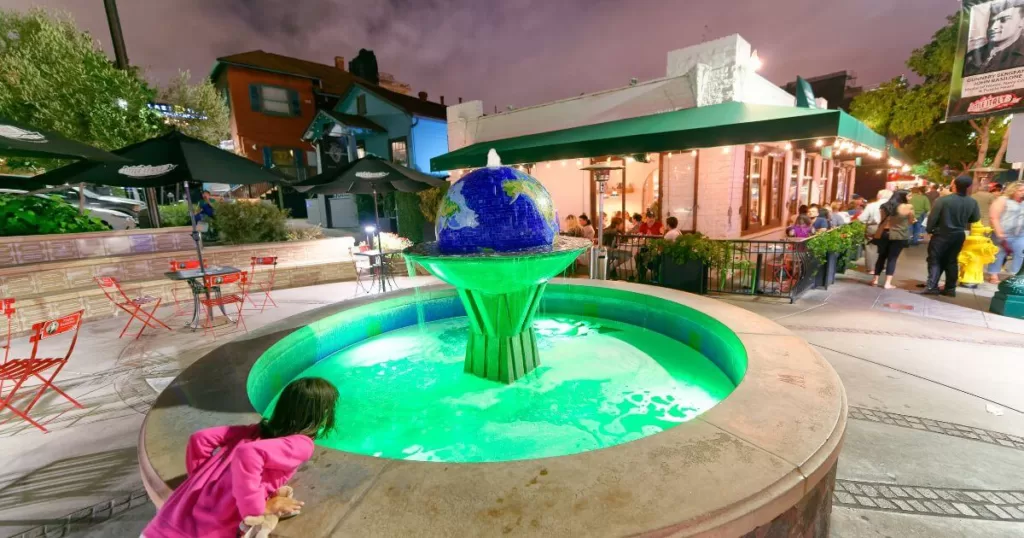 Vibrant evening in Little Italy, San Diego, with a child looking at a green-lit fountain, surrounded by outdoor dining and bustling street life, a popular thing to do in San Diego.