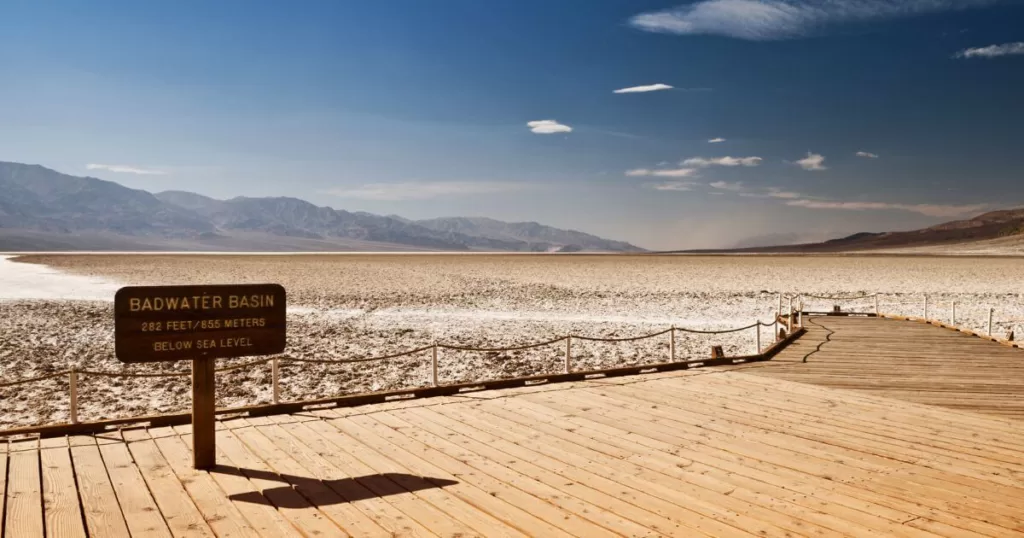 Wooden boardwalk leading to the Badwater Basin salt flats in Death Valley, one of the best National Parks on the US West Coast. This is the lowest point in North America, with a sign indicating 282 feet below sea level. 