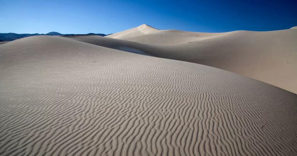 Rippled patterns on the Eureka Dunes at Death Valley National Park, with soft shadows under a clear blue sky, a serene place to visit in Death Valley.