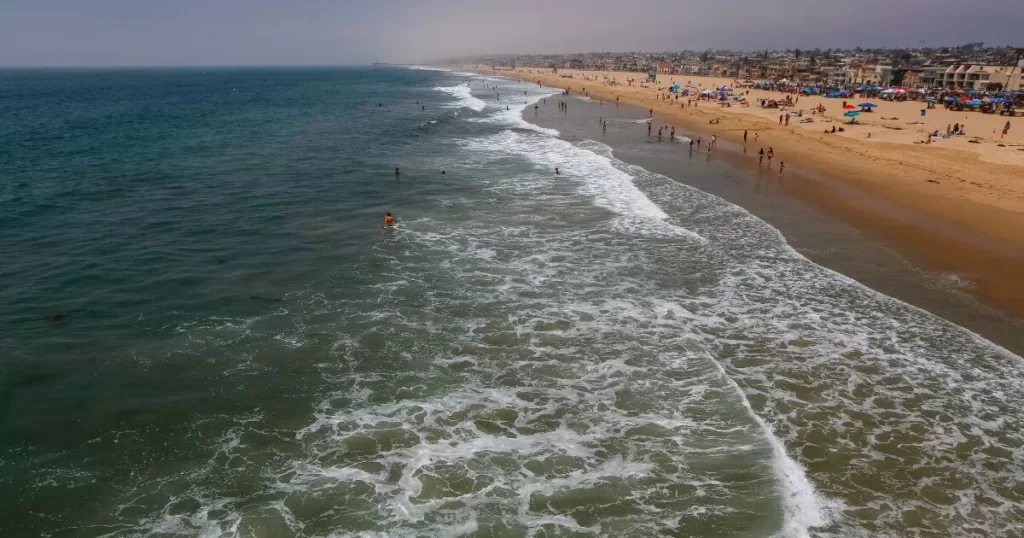 Aerial view of Hermosa Beach in Los Angeles, showcasing the long stretch of sandy beach with waves gently breaking on the shore and beachgoers enjoying the sun.