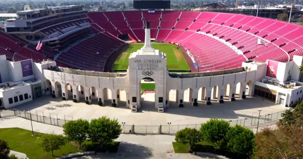 Aerial view of the historic Los Angeles Memorial Coliseum on a sunny day, showcasing its vast seating and the iconic Olympic Gateway, a symbol of the city's rich sporting legacy.