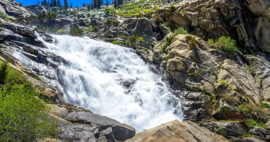 Tokopah Falls cascades powerfully over granite boulders, surrounded by lush greenery under a bright blue sky in Sequoia National Park, a magnificent sight and one of the park's natural attractions.