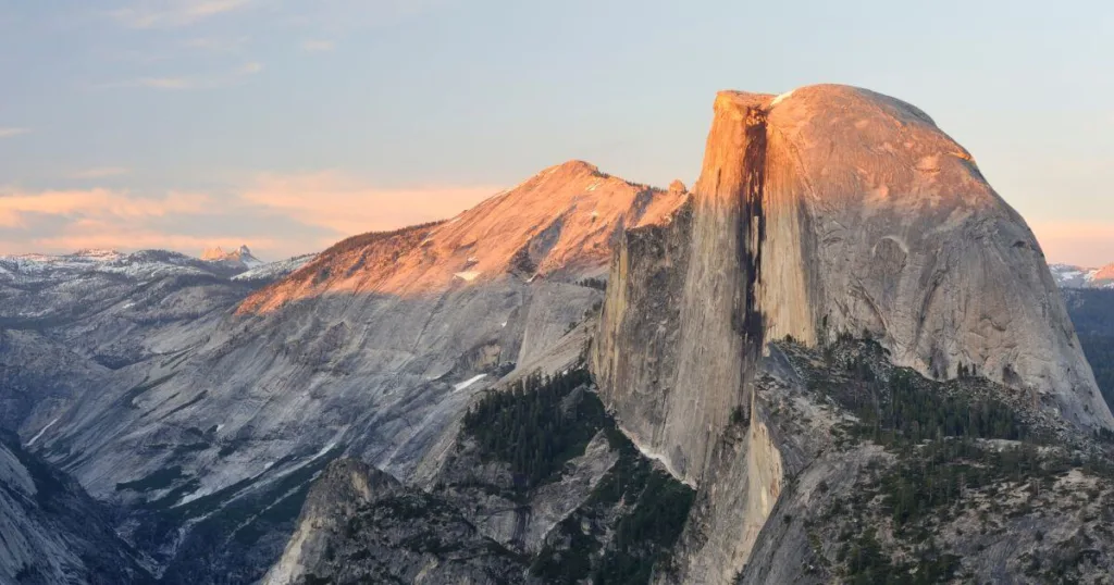 The majestic Half Dome at sunset in Yosemite National Park, its peak illuminated by the soft, golden light. Hiking to the summit of Half Dome is considered one of the best things to do in Yosemite, offering unparalleled views and a challenging adventure.