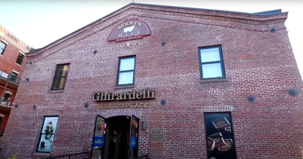 The historic brick facade of the Ghirardelli Marketplace in Ghirardelli Square, featuring the prominent Woolen Mill Building sign.