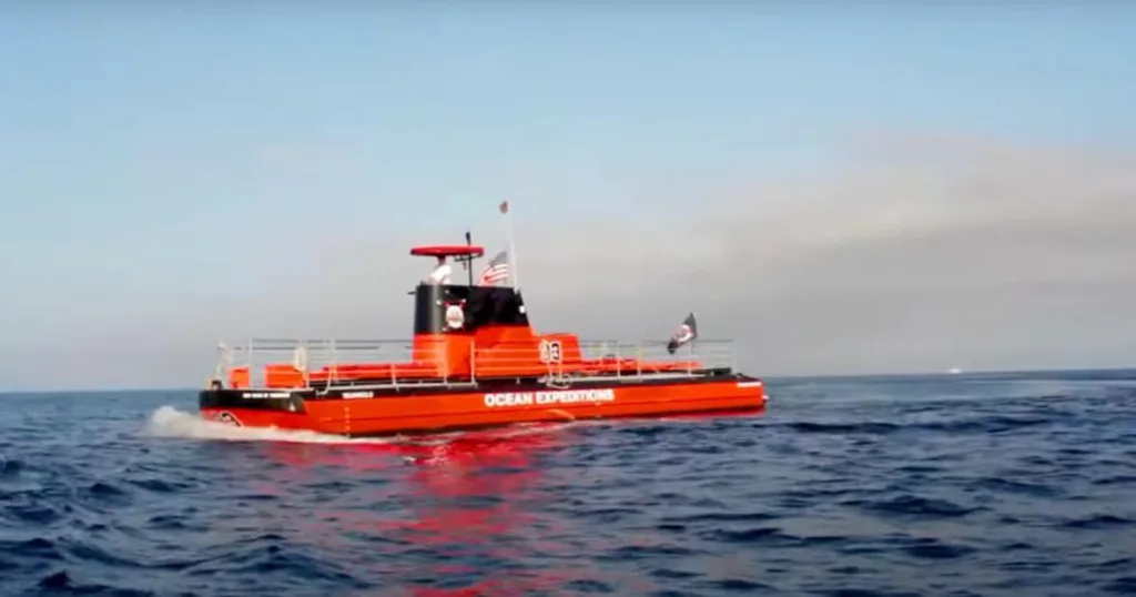 A vibrant red semi-submersible vessel labeled "OCEAN EXPEDITIONS" cruises on the surface of the ocean near Catalina Island, designed for underwater viewing to explore marine life.