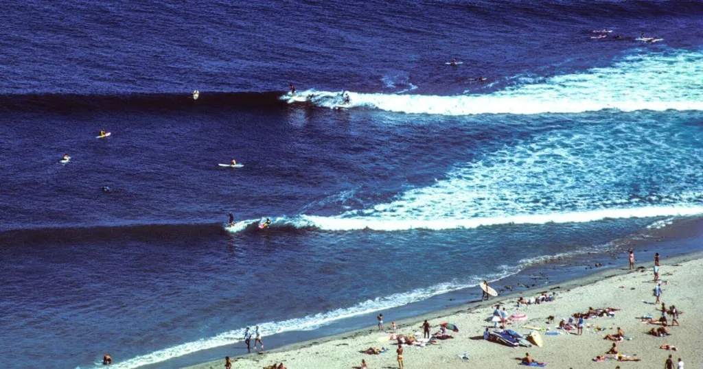 An aerial view of Surfrider Beach in Malibu, teeming with surfers and waves, a popular spot for those looking for things to do in Malibu, with sunbathers and beachgoers dotting the sandy shore.