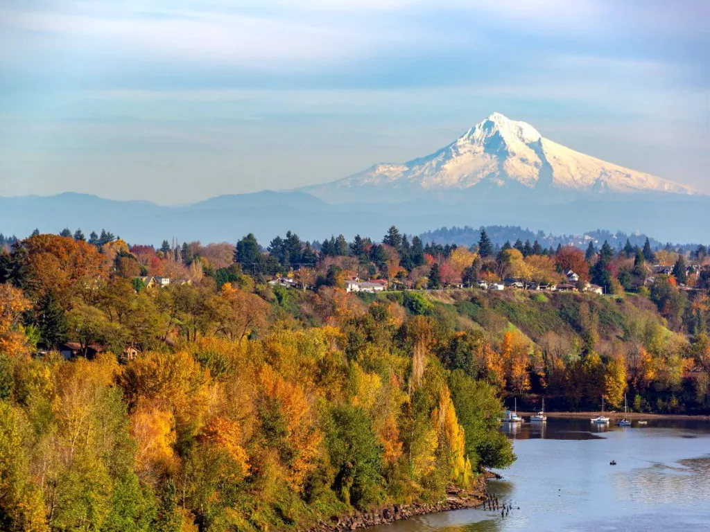 A scenic view of Mount Hood towering in the distance, its snowy peak contrasting with the colorful autumn foliage of the surrounding landscape, highlighting it as one of the stunning places to visit in Oregon.